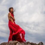 45555942 a woman in a red dress stands above a stormy sky her dress fluttering the fabric flying in the wind