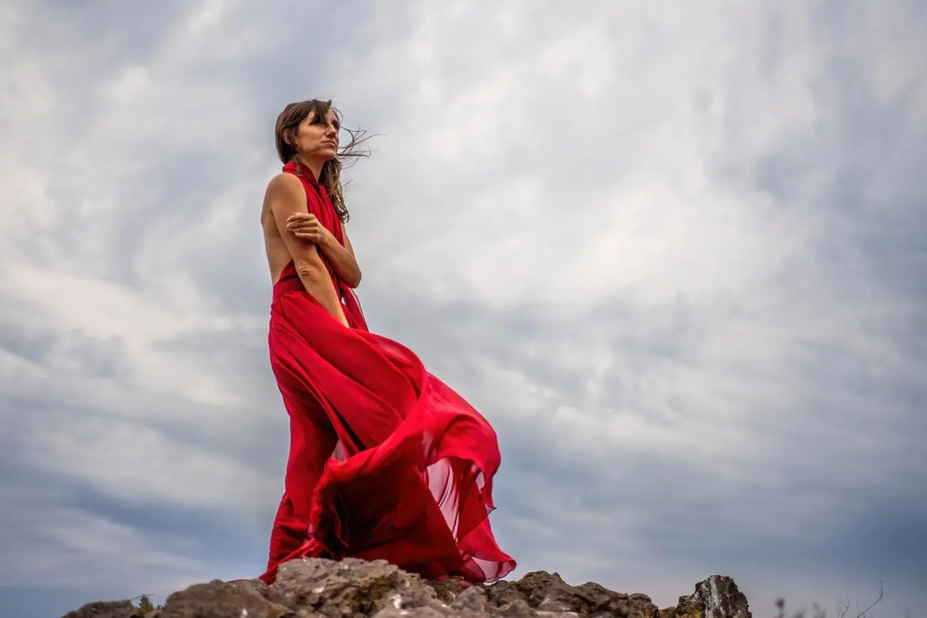 45555942 a woman in a red dress stands above a stormy sky her dress fluttering the fabric flying in the wind jpg