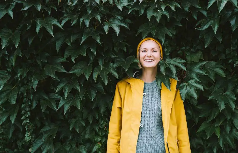 Uśmiechnięta kobieta w żółtym płaszczu na tle liści