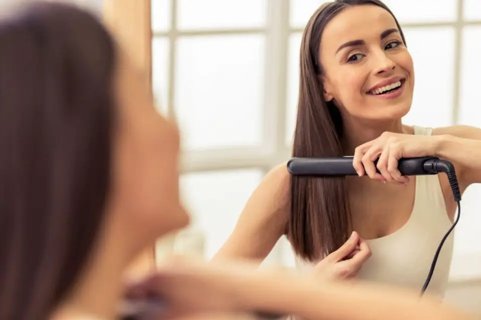 Kobieta w średnim wieku prostuje włosy przed lustrem w łazience
